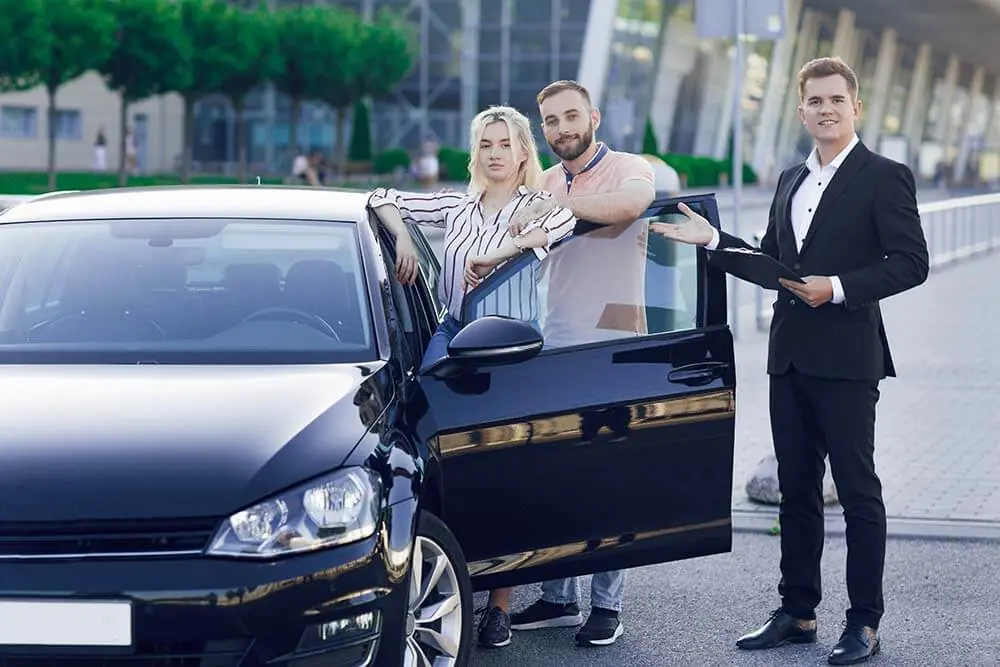 Young Car Dealer Business Suit Shows Buyers New Car Young Couple Man Woman Buy Car Purchase Machines Test Drive